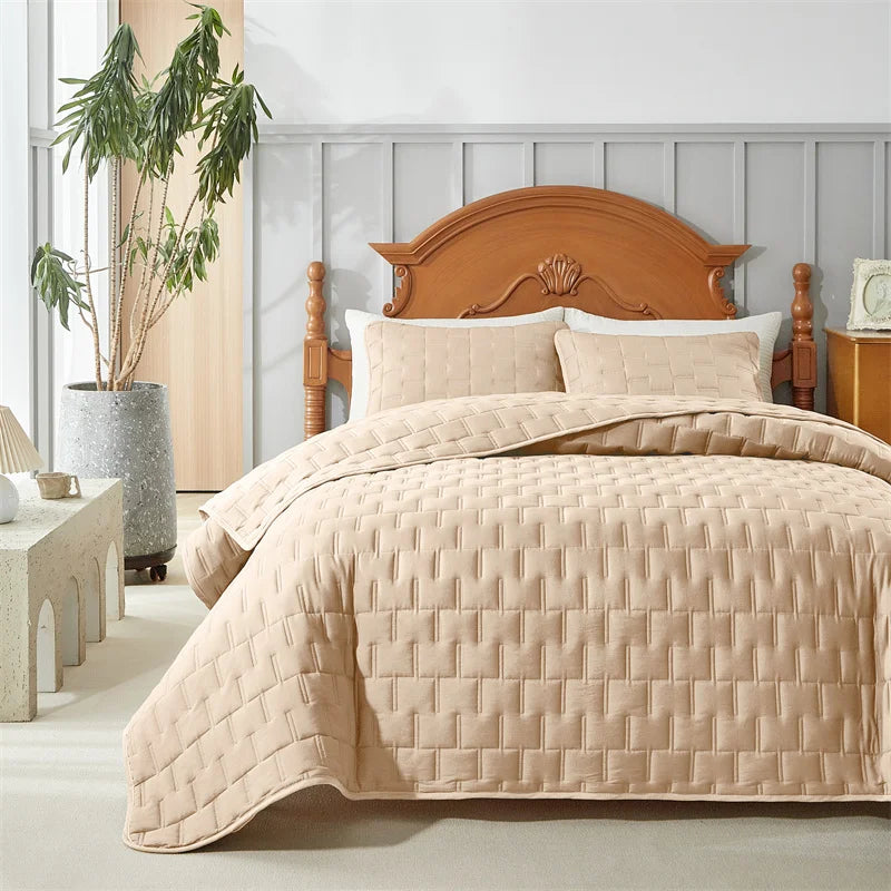 Light beige quilted bedding set with a wooden headboard and white linens in a bright room.