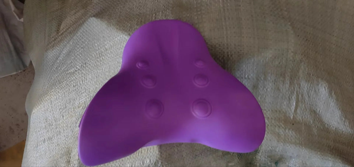 A purple cervical massage pillow is shown resting on a light-colored fabric.