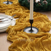 A yellow crinkled cheesecloth table runner draped across a wooden surface with a white candle and green wreath.