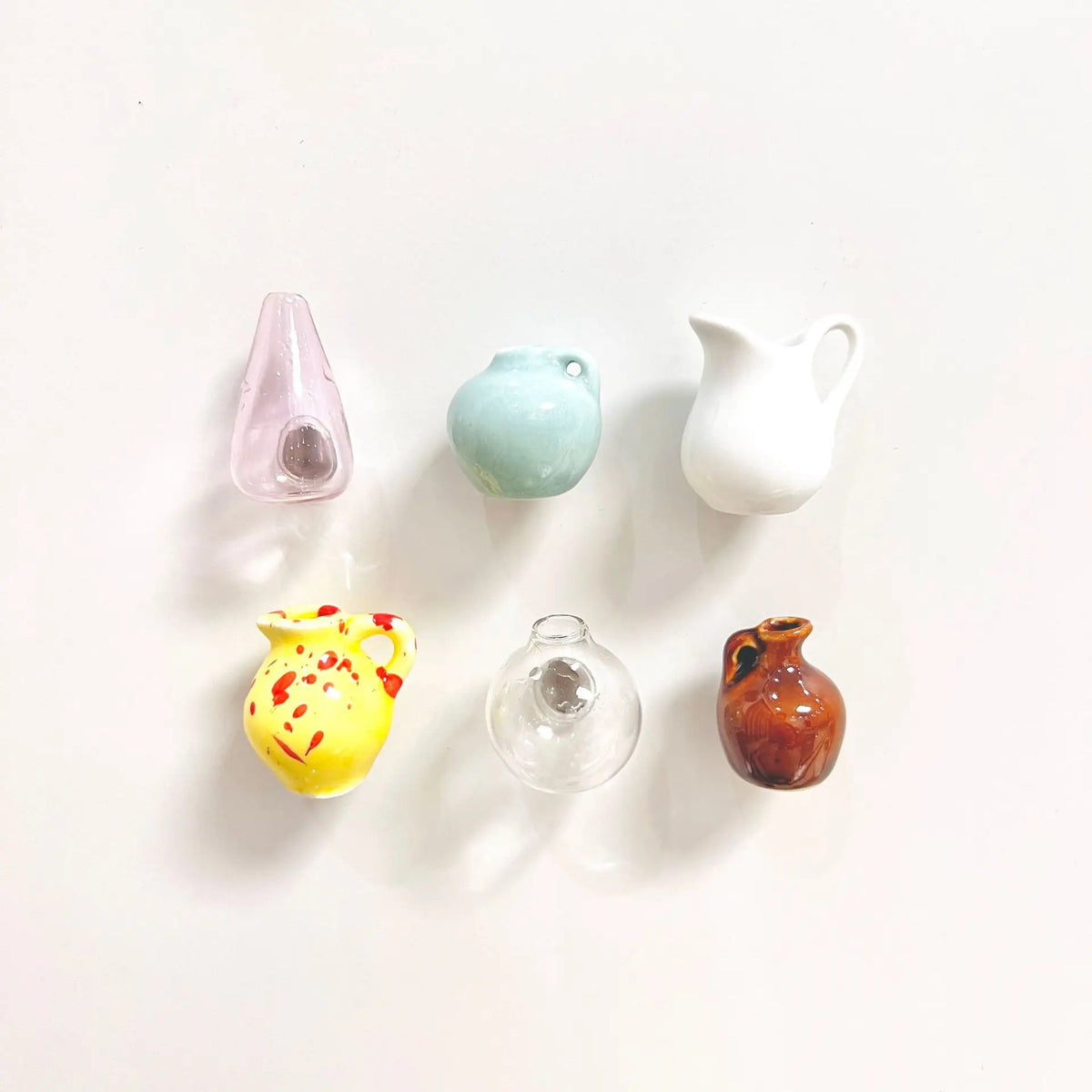 Five small ceramic landscape fridge magnets in pastel colors including pink, mint green, white, yellow, and brown.