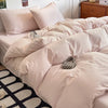 A close-up of a beige ultra-soft washed cotton quilt bedding set on a bed with light pink pillows and a black and white patte