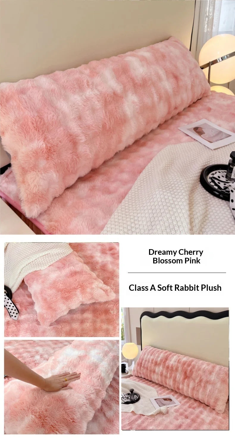 A fluffy pink rabbit plush long pillowcase displayed on a bed with a white blanket and a photo.
