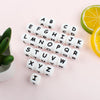 A collection of white silicone alphabet beads arranged in a scattered pattern on a light pink surface.
