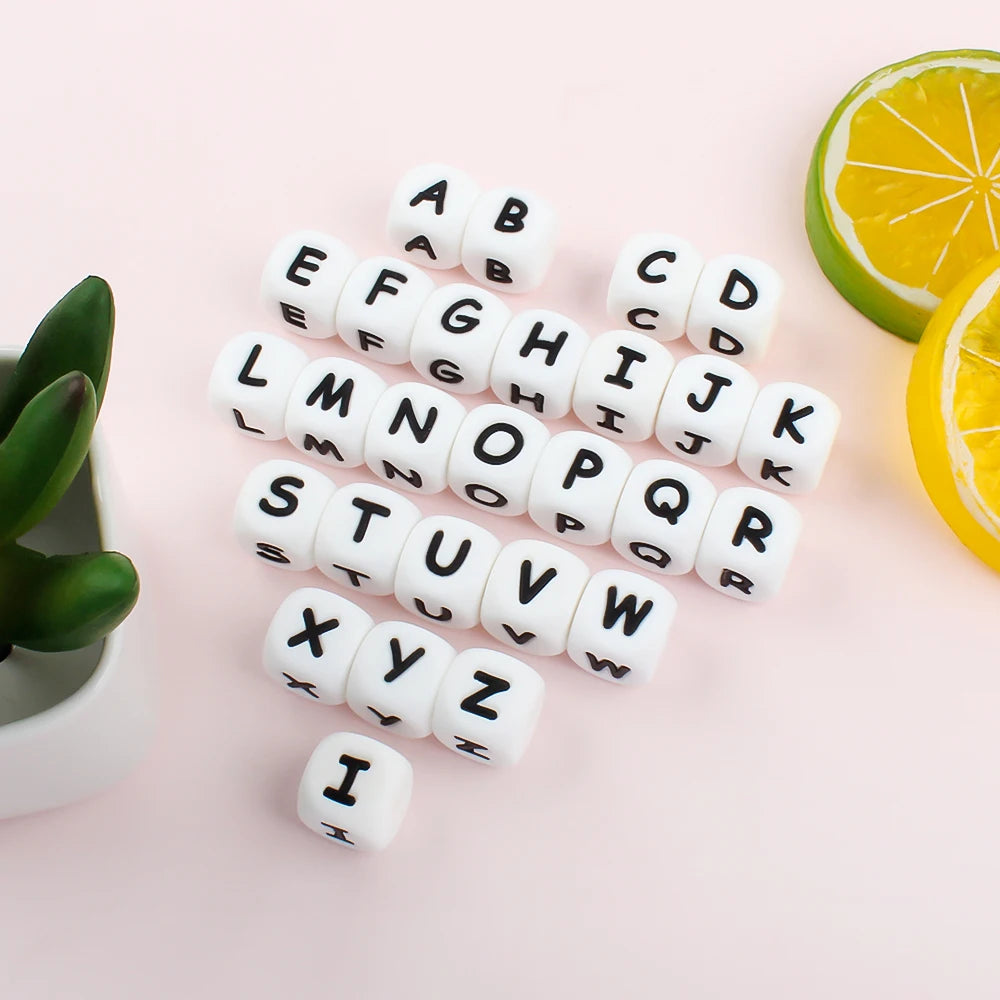 A collection of white silicone alphabet beads arranged in a scattered pattern on a light pink surface.