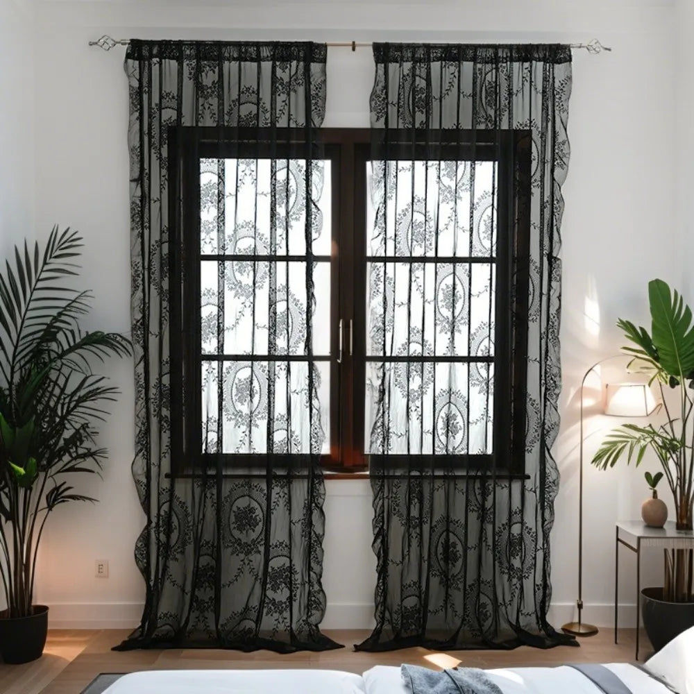 A set of black floral lace sheer curtains hanging in a window frame.
