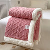 A thick pink quilted fleece blanket with white trim is folded on a white bed.