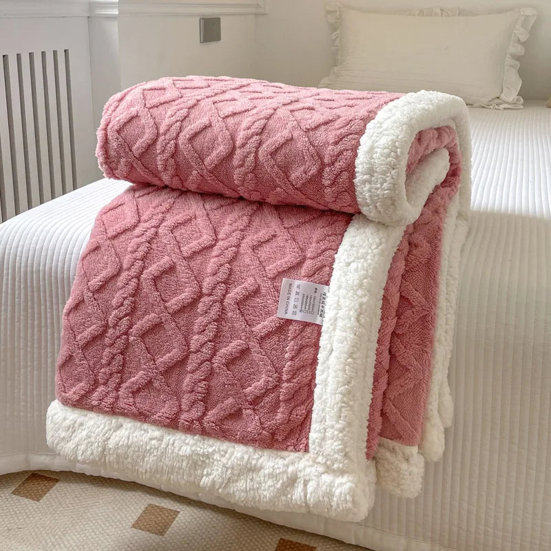 A thick pink quilted fleece blanket with white trim is folded on a white bed.
