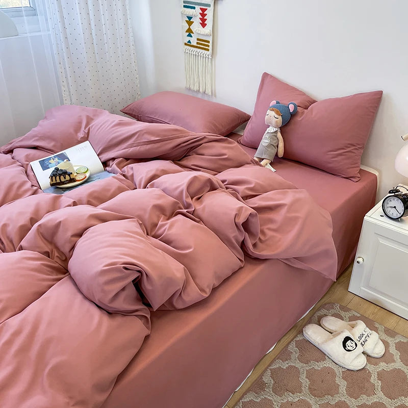A pink duvet cover set with matching pillowcases and a stuffed animal on a bed.