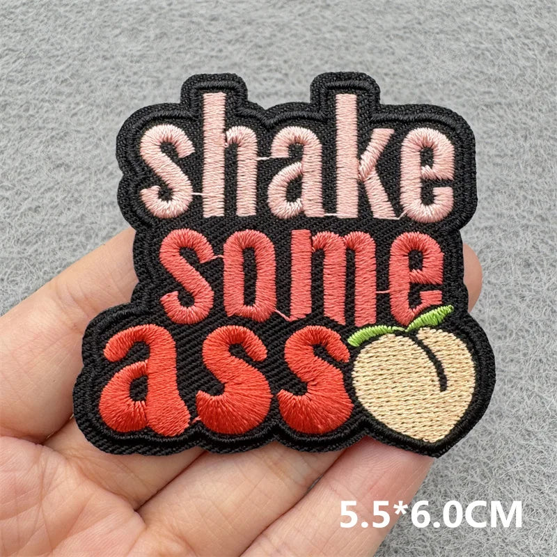 Black embroidered patch with pink and orange text that reads Shake some ass