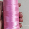 A hand holds a spool of bright pink high tenacity polyester sewing thread with a yellow plastic core.