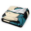 A plush decorative throw blanket featuring a stylized character design in white, teal, and black.
