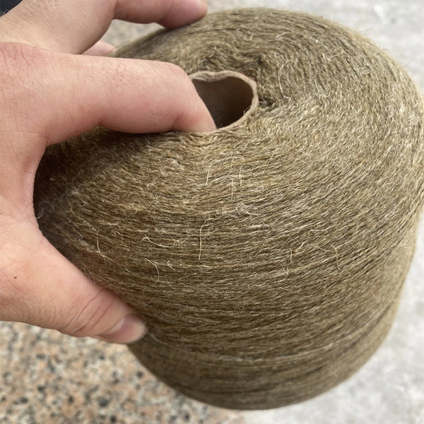 A hand is holding a ball of brown hand-woven wool and linen blended yarn.