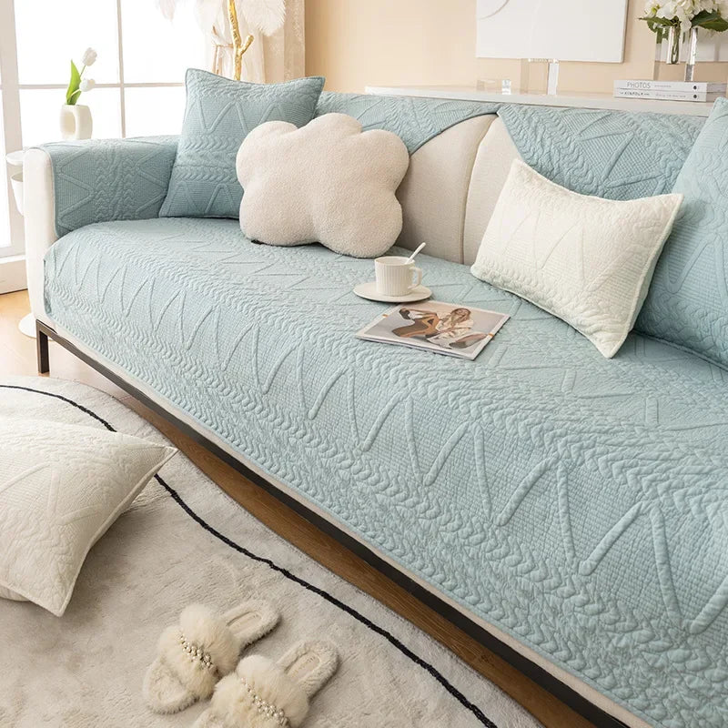 A light blue textured sofa cover with a cream cushion and decorative pillows on a wooden frame.