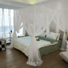 Elegant mosquito net bed canopy with sheer white fabric draped over a green bed.
