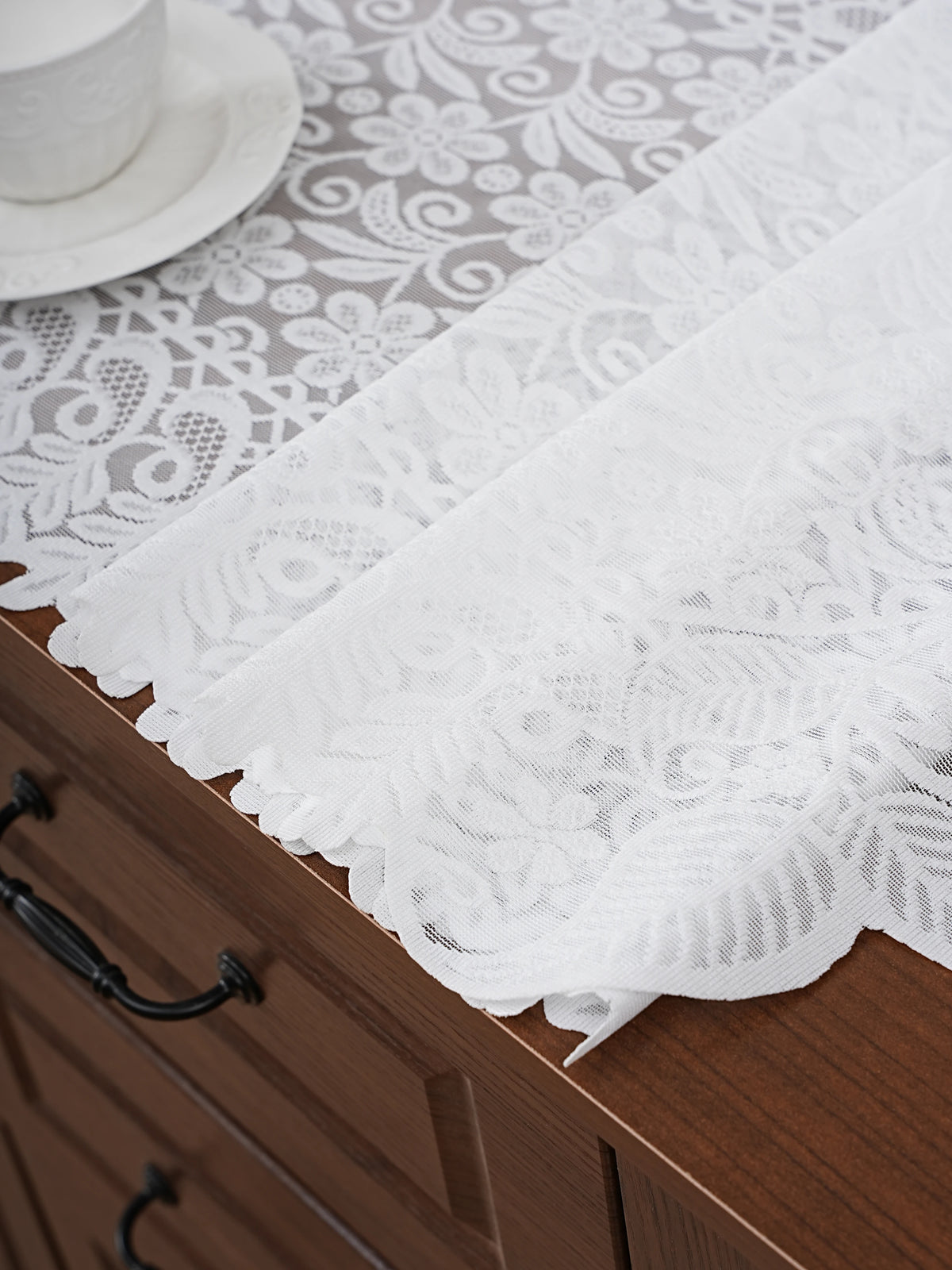 White embroidered lace table runner draped over a dark wood cabinet surface.
