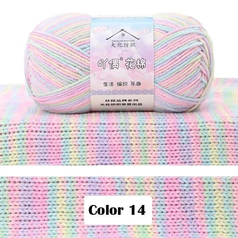 A ball of pink and blue gradient yarn labeled as DAHUAFANGZHI silk yarn resting on a pink striped knitted fabric.