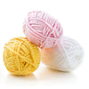 Three balls of thick velvet yarn in pink, yellow, and white stacked on a white surface.