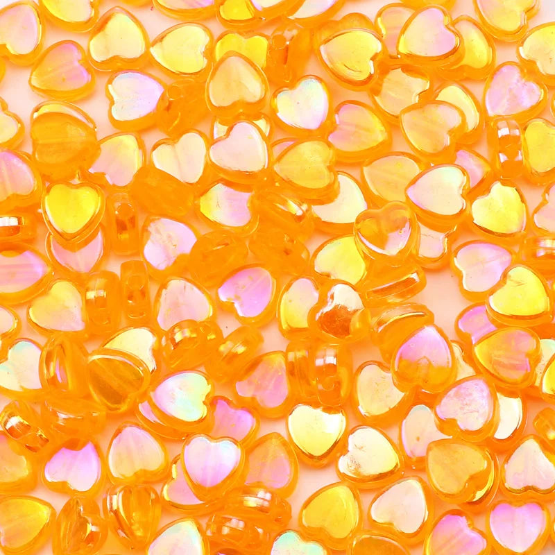 A pile of small, translucent orange acrylic heart beads for jewelry making.