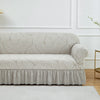 A light beige jacquard stretch sofa cover featuring a leaf pattern and a gathered bottom edge.