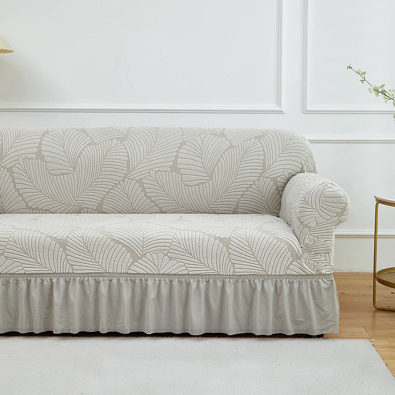 A light beige jacquard stretch sofa cover featuring a leaf pattern and a gathered bottom edge.