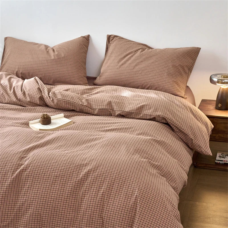 A beige plaid duvet cover set with matching pillows and a folded blanket on a bed.