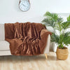 A brown shaggy blanket draped over a white sofa next to a large green potted plant.
