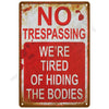 A vintage rusted metal sign with red lettering that reads NO TRESPASSING WE'RE TIRED OF HIDING THE BODIES