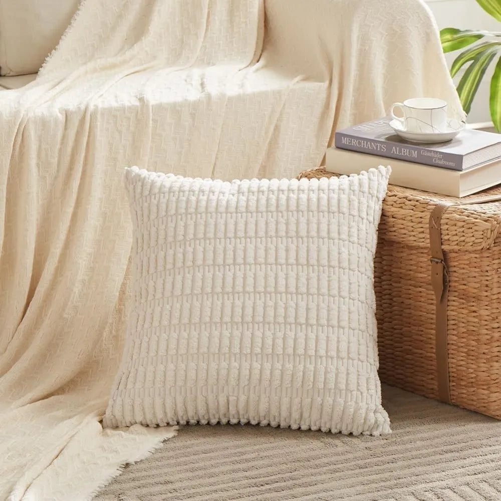 A cream knitted throw pillow resting on a woven basket next to a beige draped fabric.