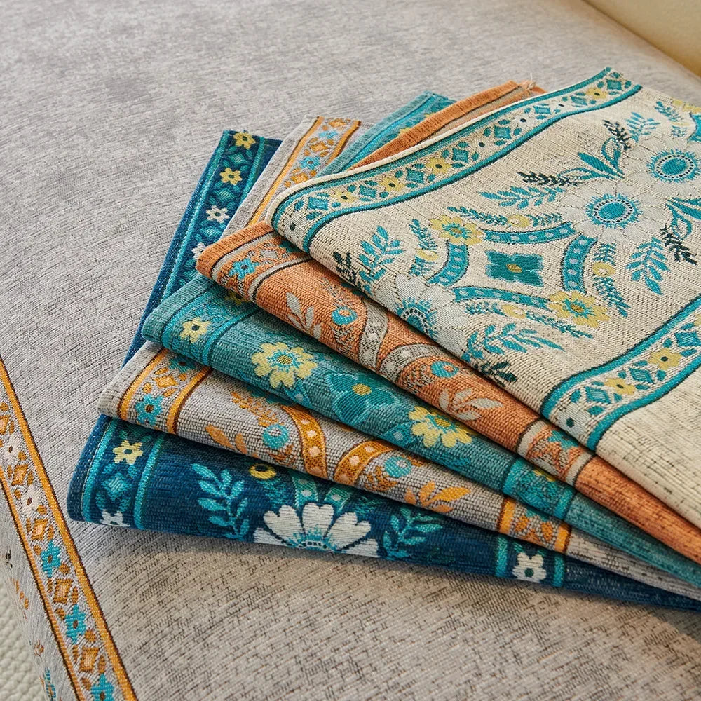 Stack of patterned chenille sofa covers featuring blue, teal, and beige embroidery.