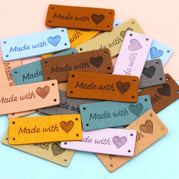 A collection of handmade leather tags in various colors including brown, yellow, gray, and pink, featuring a heart design.