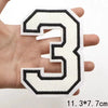 A hand holds a white and black letter patch shaped like the number three.