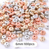 A pile of small, round geometric acrylic beads in various shades of rose gold and silver.