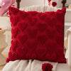 A deep red heart-patterned plush cushion cover resting on a white fabric surface.