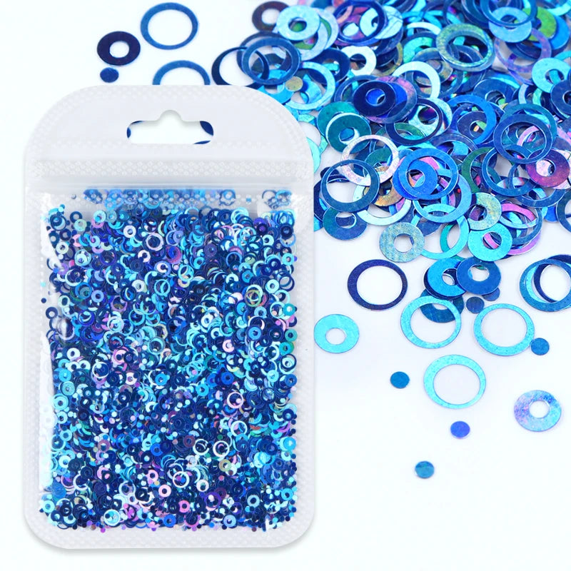A clear plastic container filled with blue and purple sparkly resin glitter filler alongside loose glitter pieces.