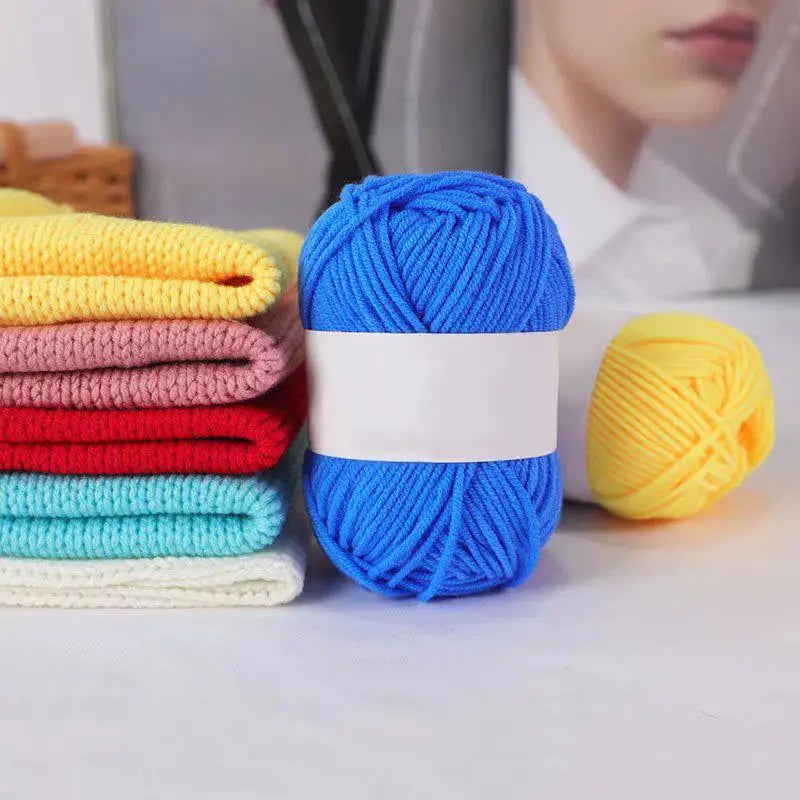 A stack of bright blue knitting yarn next to a ball of yellow yarn on a white surface.