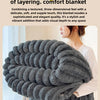 A dark gray, three-dimensional striped blanket is shown draped over a person's arm.
