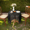 Elegant black lace tablecloth covering a small wooden table set for dining with flowers and candles.