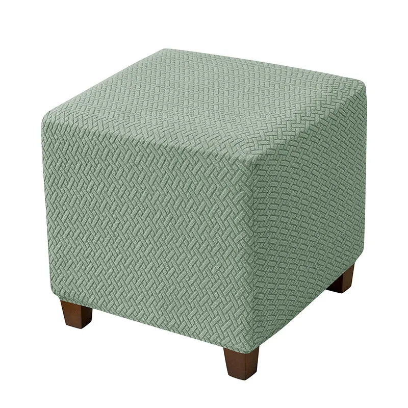 A square ottoman slipcover in a muted sage green color with a diamond pattern.
