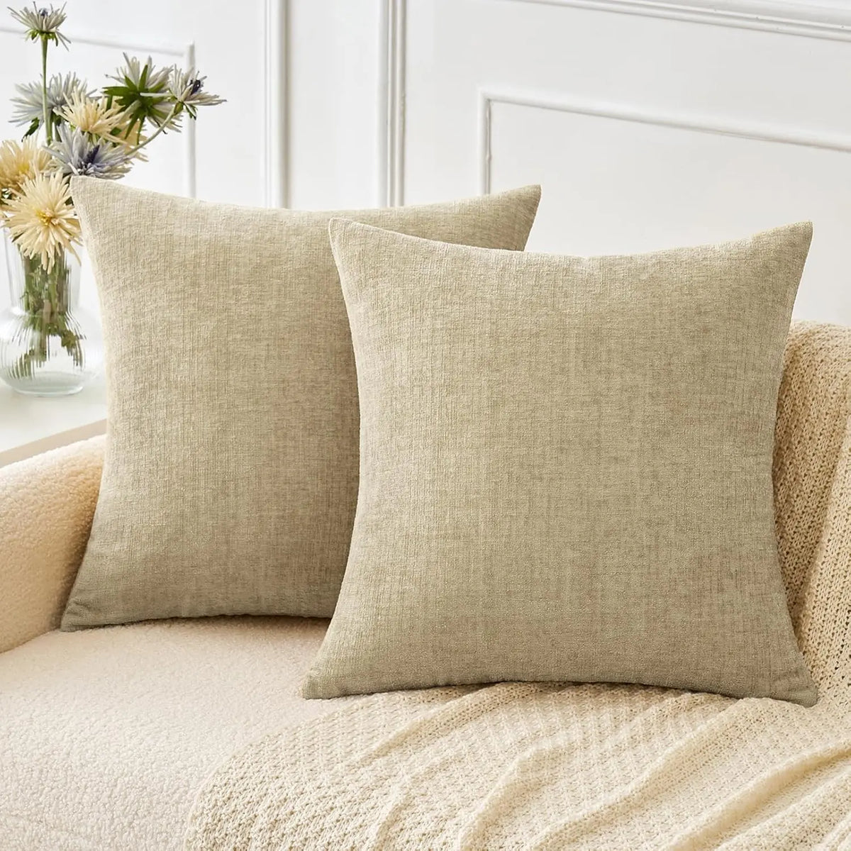 A beige chenille throw pillow cover resting on a light-colored sofa with a cream knit blanket.