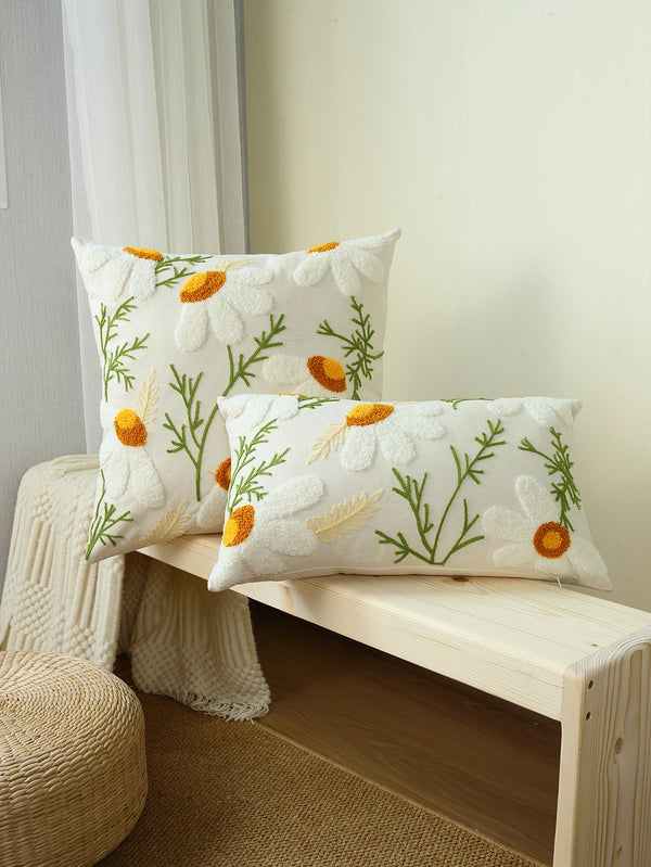 A white cushion cover with yellow and green floral embroidery resting on a light wood shelf.