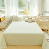 A light green and white checkered organic cotton flat sheet and pillow set on a bed near a window.