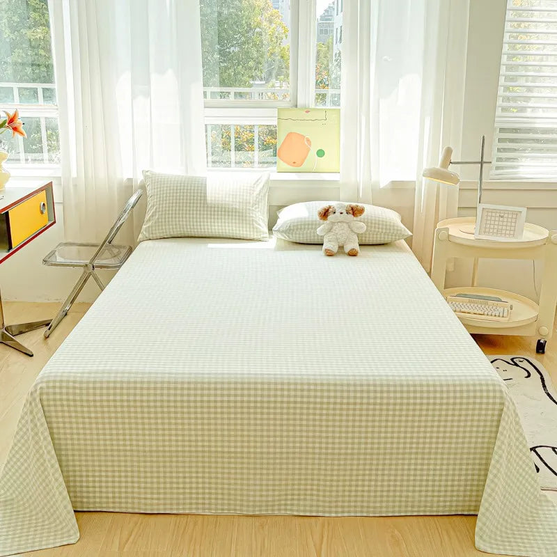 A light green and white checkered organic cotton flat sheet and pillow set on a bed near a window.
