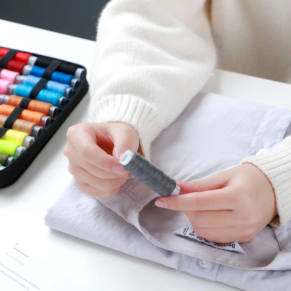 A person is using a complete sewing kit to thread a needle with gray thread on a piece of fabric.