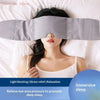 A woman is using a gray weighted sleep mask on her eyes while lying in bed for relaxation and immersive sleep.