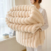 A woman holds a fluffy, cream-colored blanket made of thick, soft wool fibers.