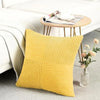 A yellow corduroy patchwork pillow cover resting on a gray rug next to a white sofa and a wooden table.