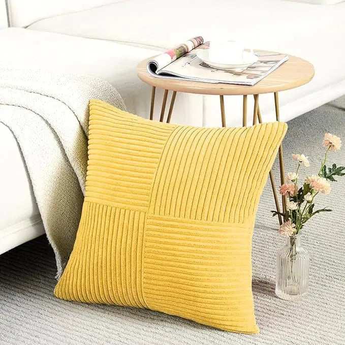 A yellow corduroy patchwork pillow cover resting on a gray rug next to a white sofa and a wooden table.