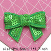 A bright green sequin bow made of fabric is shown against a pink grid background.