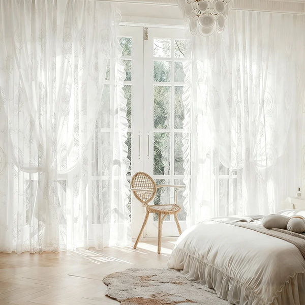 White sheer ruffled lace embroidered curtains framing a bright window and a light wood floor.