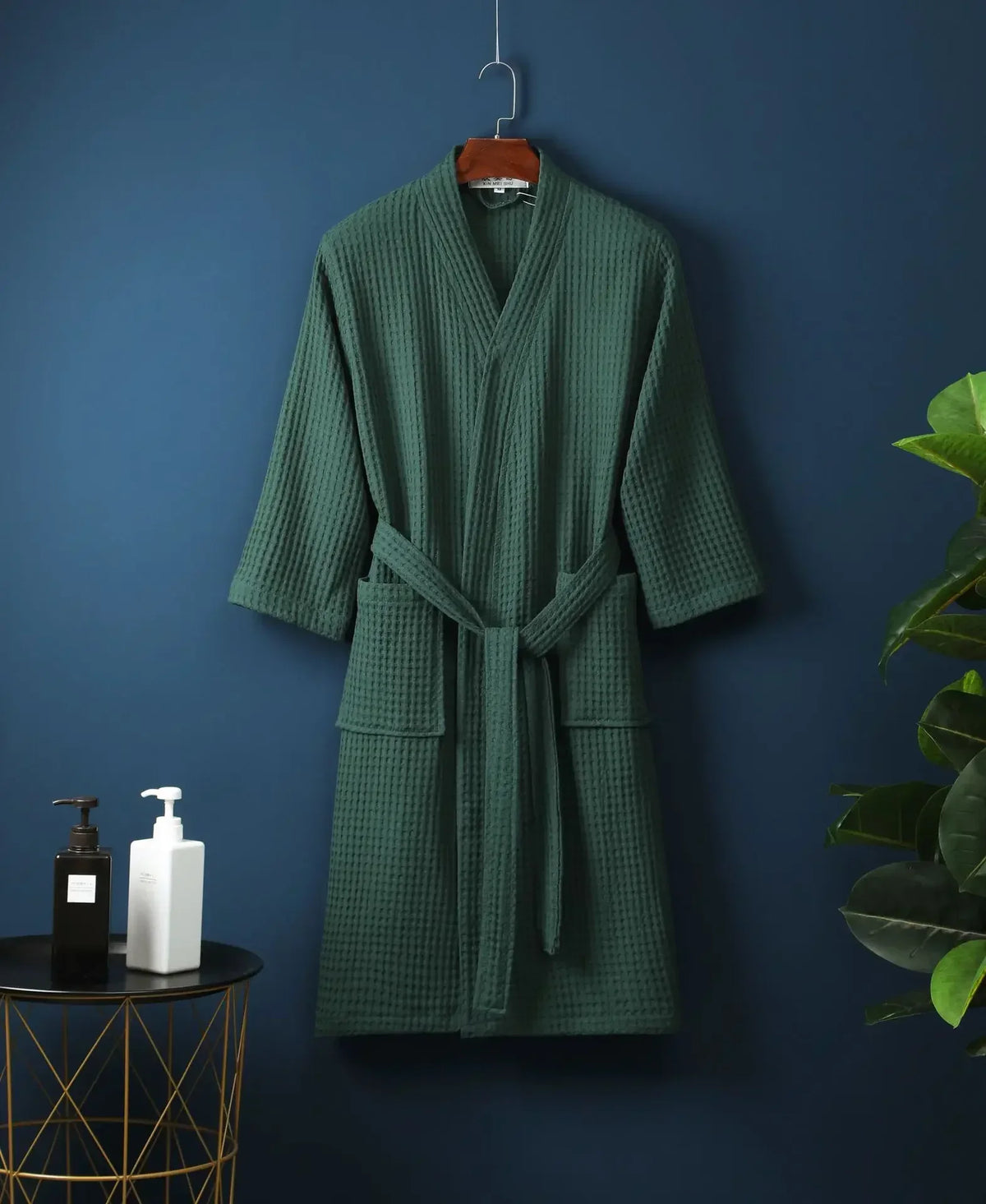 A dark green cotton terry robe hanging on a wall against a deep blue background.